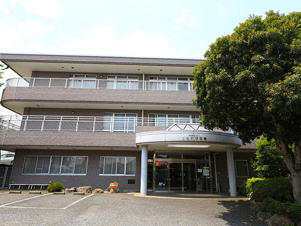 3階建てのレンガ造り介護施設の建物外観。玄関部分と緑化が見える。